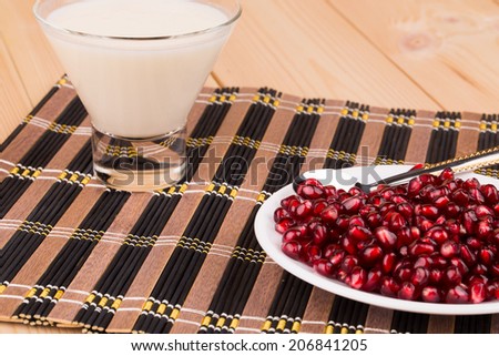 red grains of a pomegranate and milk on the wooden background