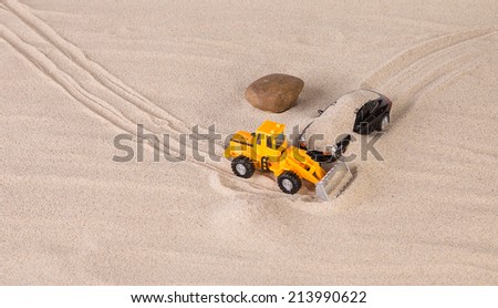Concept of yellow loader and black car. Sand background.