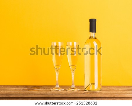 Bottle with white wine and glasses on wooden table. Yellow background