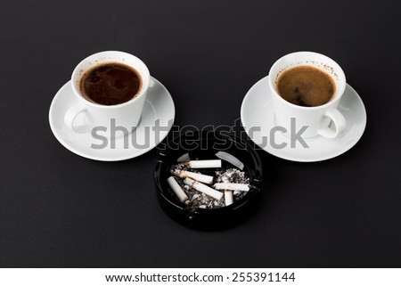 Cups of coffee with ashtray with cigarettes on the black background
