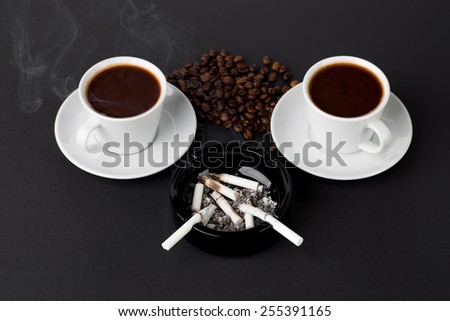 White cups of coffee with ashtray and coffee beans on the black background