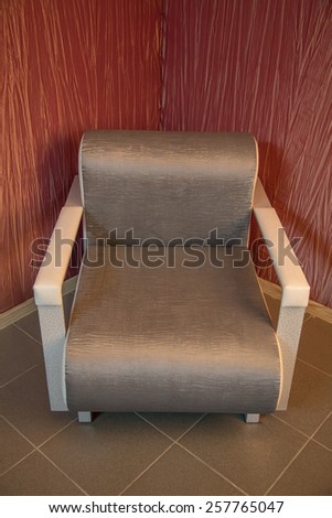 Stylish empty armchair standing in the corner of a room with wallpapered walls