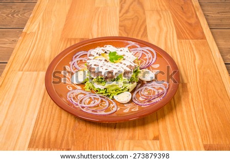 Beef steak tartare with white sauce and garnish. Plate located on wooden table background.