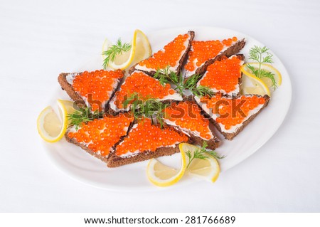 Rye bread with butter and red caviar with lemon and dill as a sandwich. Plate located on a white canvas tablecloth background.