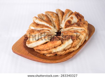 Delicious sliced puff pie with curd cheese and cabbage. Wooden platter located on a white canvas tablecloth background.