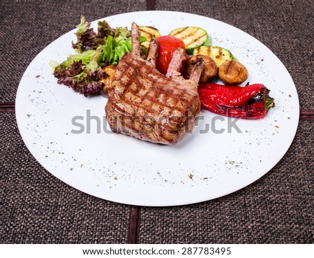 Delicious lamb racks with griled vegetables. Plate located on a brown tablecloth background.