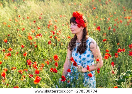 Beautiful romantic lady on the poppy field dressed in casual dress and floral wreath. Summer shot at sunset.