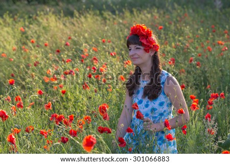 Beautiful romantic lady on the poppy field dressed in casual dress and floral wreath. Summer shot at sunset with backlight..