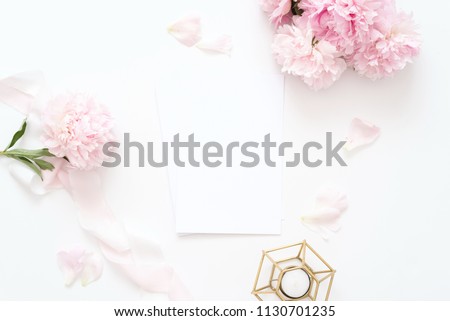 Styled feminine top view.on white background with wedding card, pink peonies petals, candle