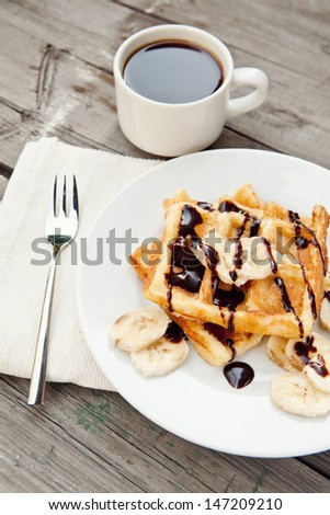 Breakfast : waffles with bananas, chocolate syrup and coffee. Selective focus