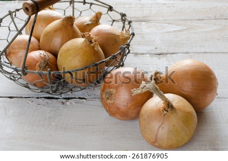 Yellow onions in a metal basket on a wooden table