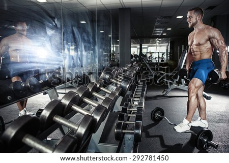 Muscular bodybuilder guy doing exercises with dumbbell in gym