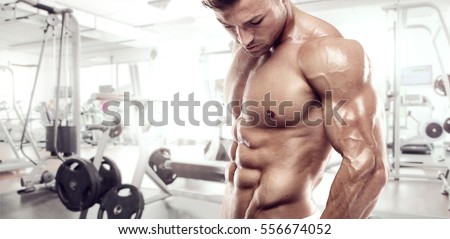 Muscular bodybuilder guy standing on gym and posing triceps muscle