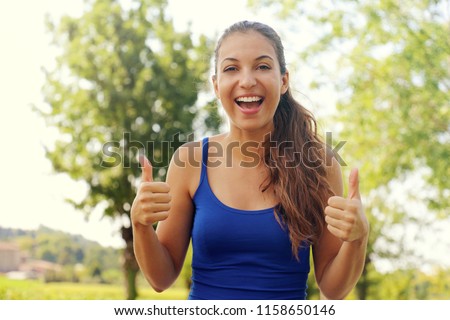 Super woman! Portrait of winner girl showing thumbs up. Positive smiling fitness woman outdoor.