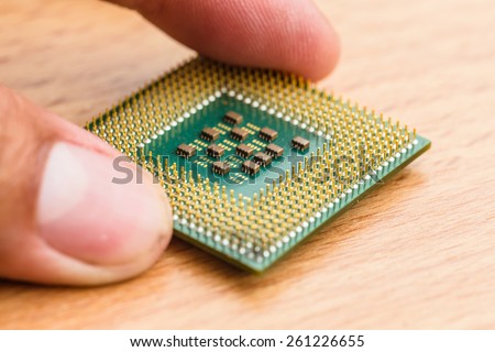 Close-up of a computer processor microchip between the fingers on wood