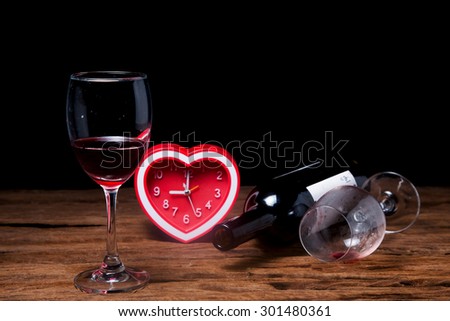 Glass of red wine with heart Clock on old brown wooden background