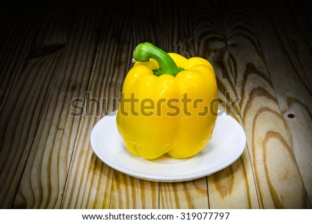 Yellow sweet peppers on a white plate on a wooden table.