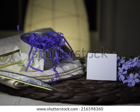 A heart gift box with shredded blue paper coming out of it, it is next to blue flowers and a blank note - homey & night feeling