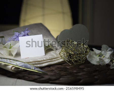 A blank note & white flowers laying on a nice textile near a golden heart box next to white flowers
