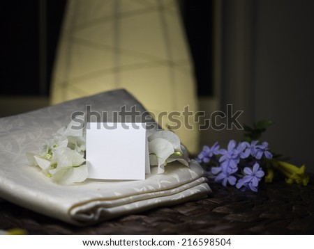 A blank note with white flowers laying on a textile near blue flowers - homey & night feeling