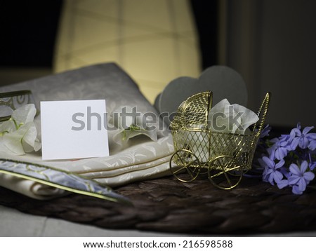 A blank note & white flowers laying on a nice textile near a golden stroller with white flowers in it next to blue flowers - homey & night feeling