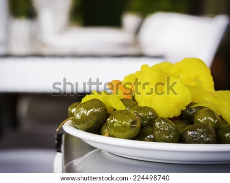 Pickles (olives, carrot and yellow cauliflower) on a white plate and a blue table - close up