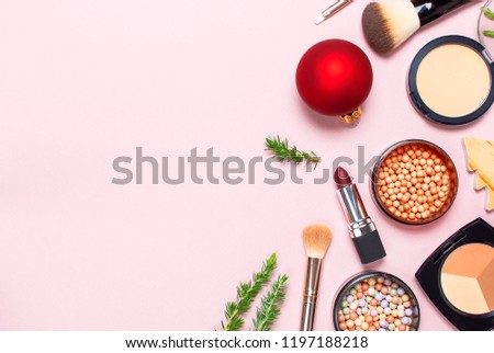 Various cosmetic products for make-up, blusher, powder, brushes, lipstick, eyeshadow and Christmas gift, fir branches, red ball on pink background Flat lay top view New year concept, winter decoration