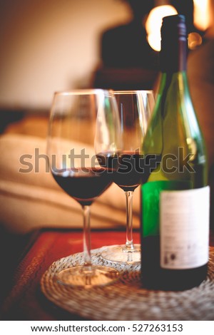 Bottle of red wine with two glasses on red table in dark romantic room candle light