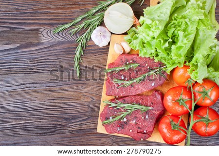 Raw beef steak on cutting board with vegetables and spices on brown wooden background