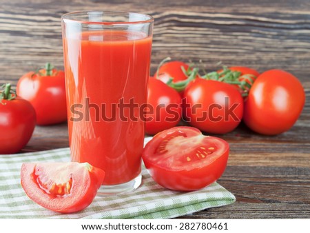 Glasses of tomato juice and fresh tomatoes on brown wooden table