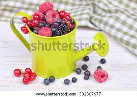 mixed berries in a small light green decorative watering can on white  wooden background