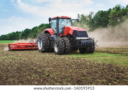 modern red tractor in the agricultural field; mechanism. Tractor plowing land. \
Harvester sowing wheat.