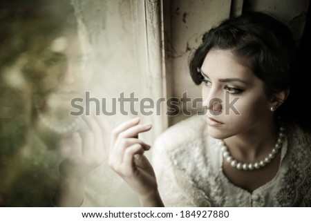 Gorgeus brunette woman with brown eyes wearing pearls looking through the window portrait