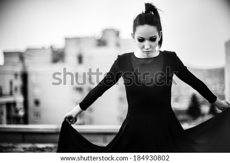 Brunette skinny woman in high fashion dress on roof top in designer dress and unique make up posing in black and white