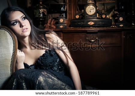 Gorgeous sexy brunette woman in vintage interior with vintage closet and old clock in background  and makeup sitting in a chair portrait
