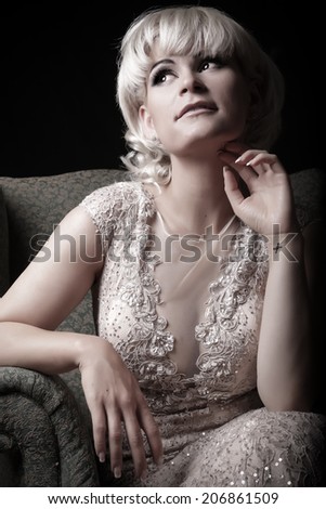 Young woman portrait sitting in a vintage chair in a elegant dress. Closeup beauty studio shoot. Healthy clean skin and glamorous makeup on beautiful face of model with short blonde hair