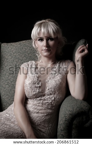 Young woman portrait sitting in a vintage chair in a elegant dress. Closeup beauty studio shoot. Healthy clean skin and glamorous makeup on beautiful face of model with short blonde hair