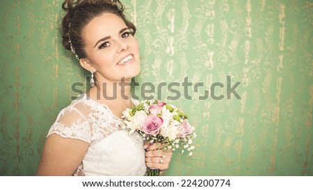 Gorgeous bride portrait in her wedding dress holding her wedding bouquet . Beautiful bridal makeup and hairstyle and accessories. Bride to be smiling portrait on the vibrant green background