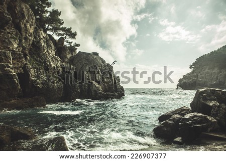 Mediterranean rocky shores and landscape - Odysseus cave on island Mljet near Dubrovnik, tourist attraction, Croatia. Young man jumping from the cliff in distance. Cliff jumping recreation on seaside
