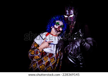 Crazy ugly grunge evil clown in town on Halloween making people shock and scared. Crazy ugly grunge evil clown and black demon nocturne mask. Scary professional Halloween masks. Halloween party