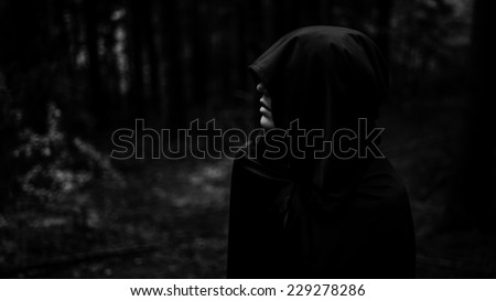 Dark demon in dark forest. Grim reaper in search of his victim. Death coming for his soul. Woman devil in black cape and hood