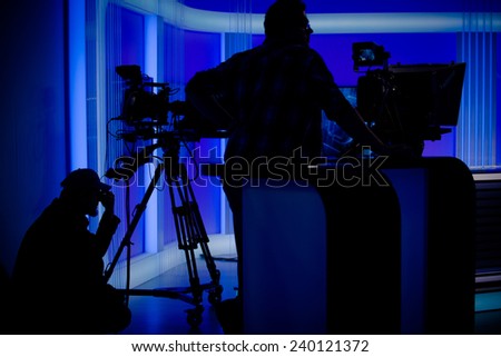 Cameraman silhouettes on a live studio news stage.Professional cameraman with headphones with camcorder in television news broadcast.Camera operators working with big broadcasting cameras