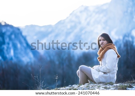 Beautiful girl in the winter coat,snowy mountains in the background.Pretty young woman tourist.Pretty woman walking in snowy mountains,wintertime recreation,trekking and hiking concept