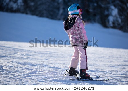 Young girl standing on skis on the slopes on a sunny morning in snowy mountain.Child at a ski resort in the mountains.Ski school.Winter vacation