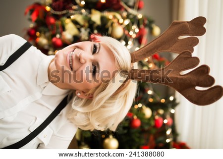 Christmas reindeer hair accessory smiling happy woman portrait with Christmas tree. Happy Christmas and New Year.Sexy seductive woman wearing her reindeer headband in warm cozy home
