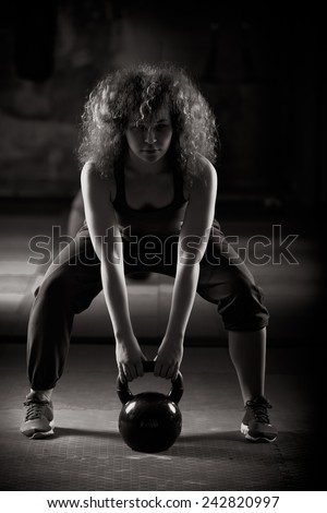 Low key fitness woman working out with kettle bell.Woman doing deadlift.Young adult fitness woman doing swing exercise with a kettlebell as a part of a fitness workout.Kettle bell workout