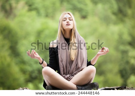 Beautiful young blonde woman meditating outdoors.Yoga woman on green grass.Calm woman meditating sitting in a park with closed eyes.Sport, meditation, park and lifestyle concept-woman meditating