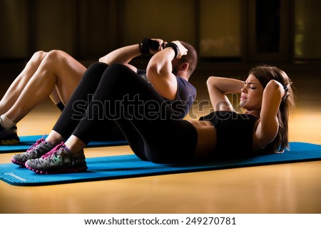 Attractive man and woman athletes performing sit ups on yoga mat.Doing sit ups, stomach muscle definition.Working in pairs.Beautiful young sporty athletic couple doing exercises together.