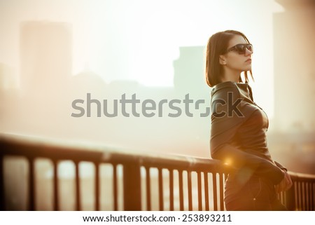 Rocker,punk woman.Young rock woman in black leather jacket casual standing with city background at sunset.Rock bad girl.Sexy attractive woman with punk rock fashion styling.Image toned and noise added