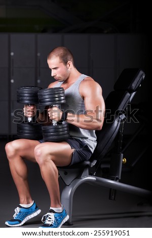 Handsome attractive muscular man training in the gym.Young muscular man doing exercises for hand muscles with dumbbell at the gym on Scott bench